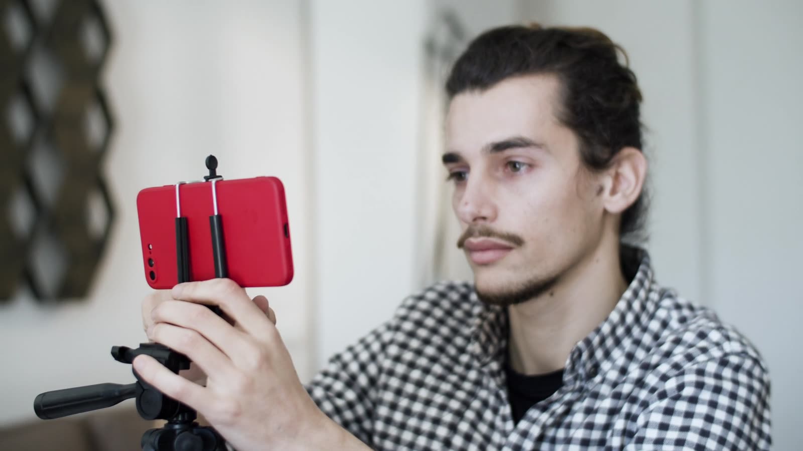 Produtor ajustando um celular vermelho no tripé para gravar conteúdo